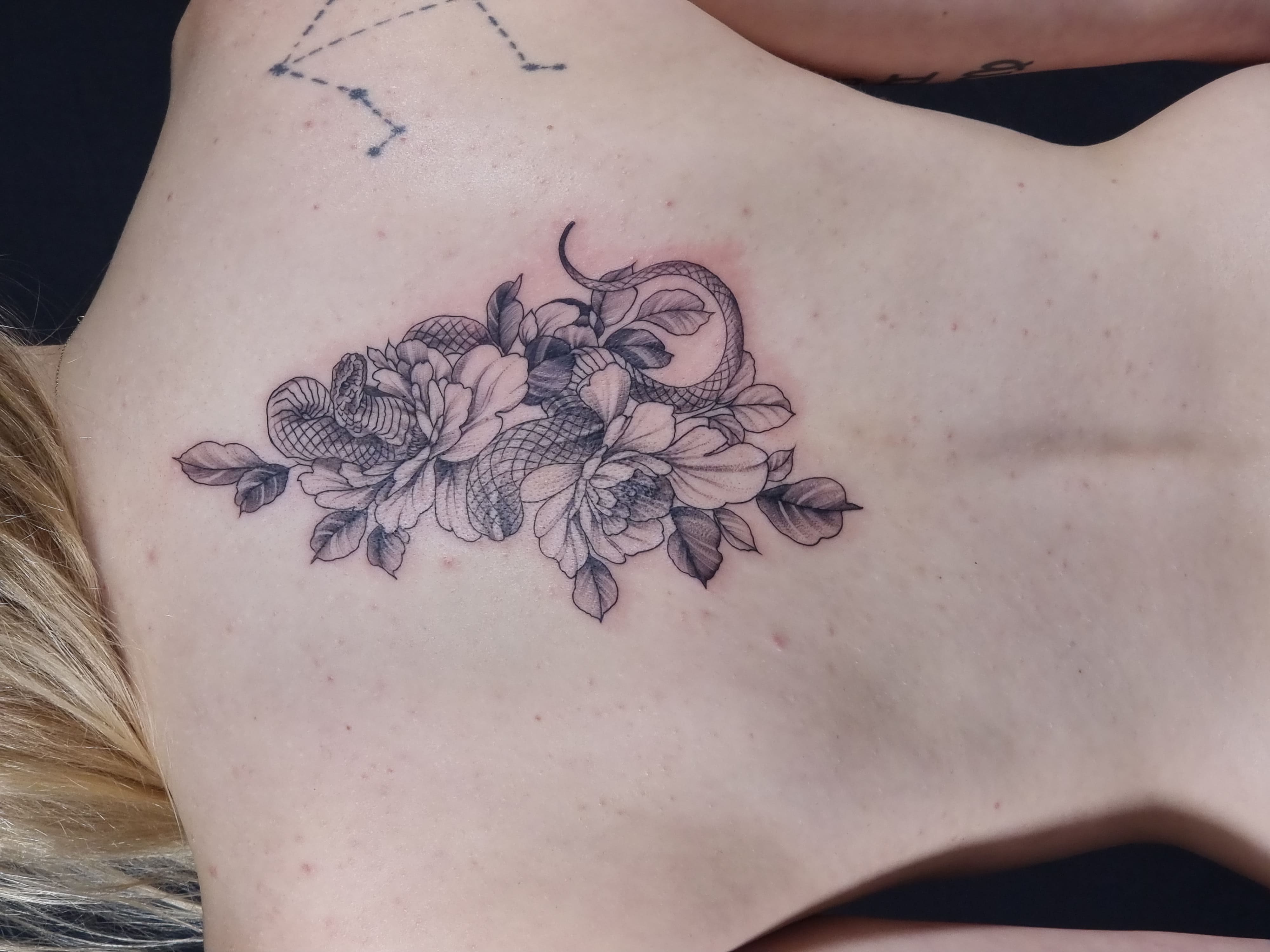 Delikatny tatuaż na plecach – kwiaty i wąż